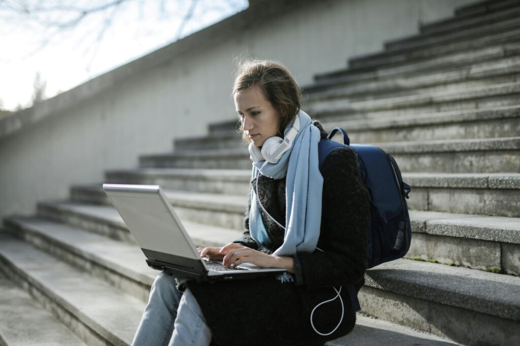 A student on a school's staircase with a laptop and backpack